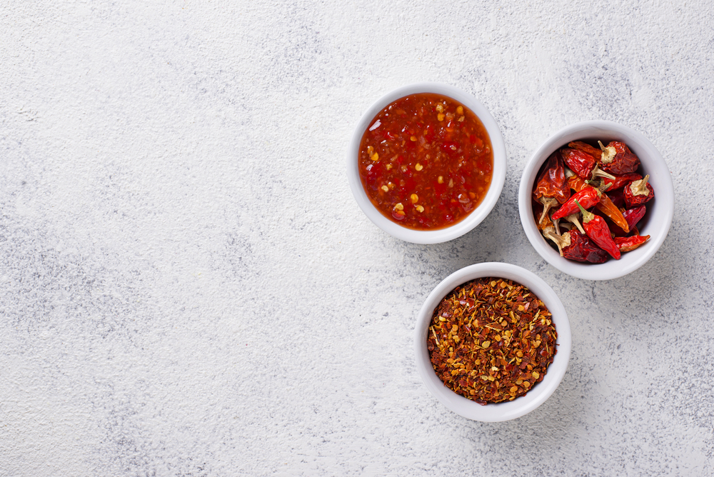 Drei Schälchen mit Chili Sauce sowie getrockneter Chili und Chiliflocken