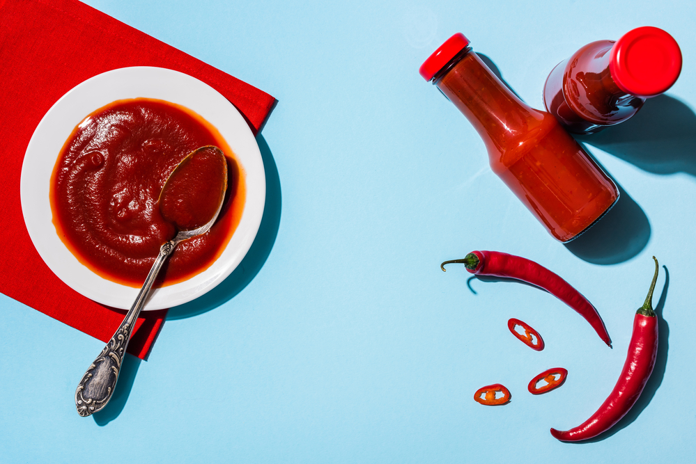 Weißer Teller und Glasflasche gefüllt mit Chilisauce auf blauem Hintergrund