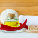 Kleine Glasflasche mit einem Öl, rote Chillischote, Massagebürste, Haarbürste und ein weißes gerolltes Handtuch