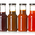 Vier verschiedene Saucen in Glasflaschen vor weißem Hintergrund