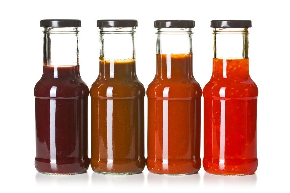 Vier verschiedene Saucen in Glasflaschen vor weißem Hintergrund