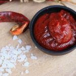 Dunkles Schälchen mit roter Sauce, daneben grobes Salz und eine Chili